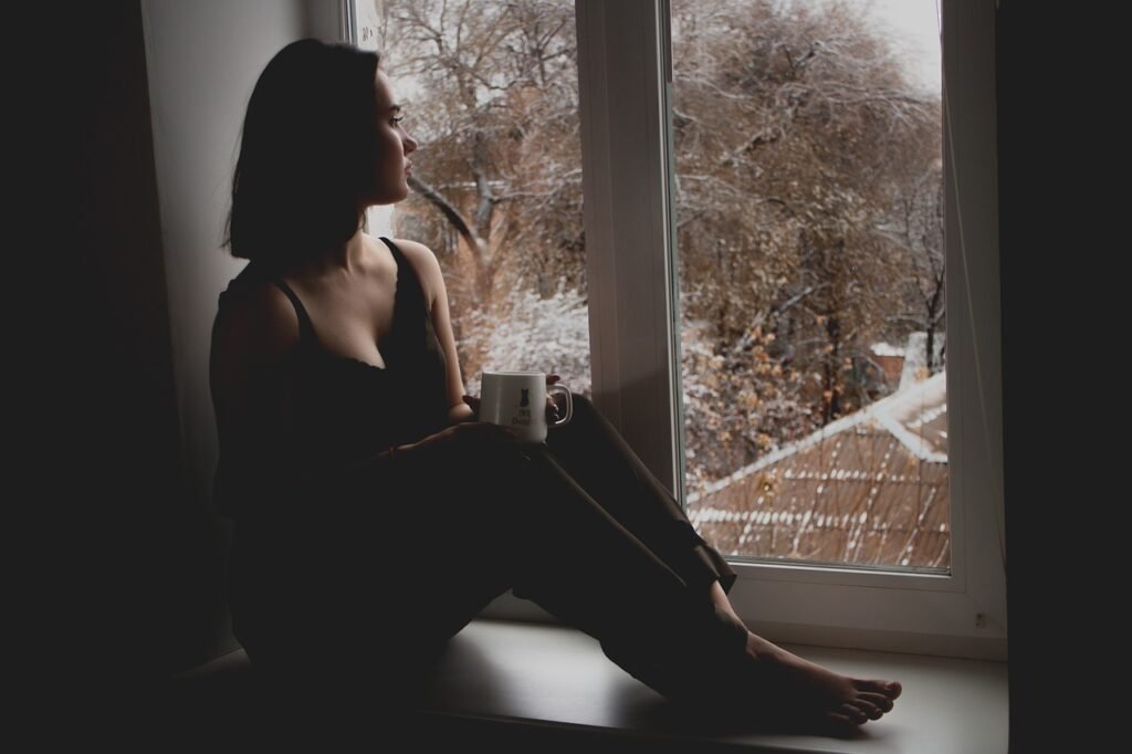 Woman sitting by a window, looking thoughtful.